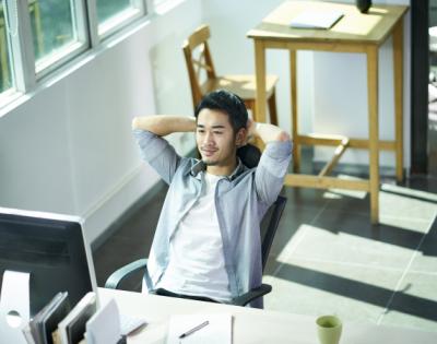 Man sitting at desk with arms behind his head in a relaxed position