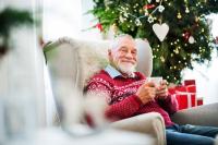 Elderly man sitting in front of Christmas tree with cup of coffee smiling